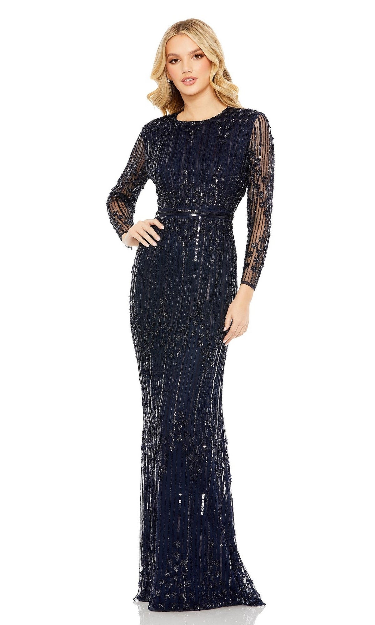 A woman poses confidently in the Mac Duggal 93781 Long Sleeve Beaded Formal Gown, a navy blue evening dress featuring sheer sleeves and vertical sequin embellishments.